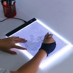 a person is drawing on a sheet of paper with a light up frame and some pens