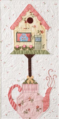 a quilted wall hanging with a teapot and house on it