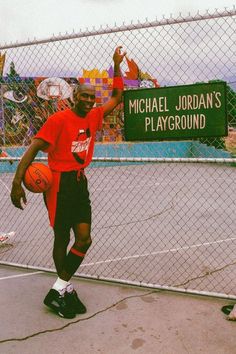 a young man holding a basketball on top of a basketball court next to a fence