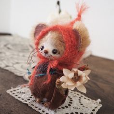 a small stuffed animal holding a flower on top of a lace doily covered table