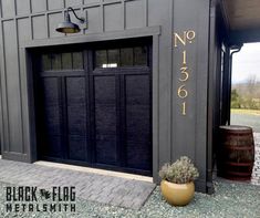 a black garage door with gold numbers on it and a potted plant next to it