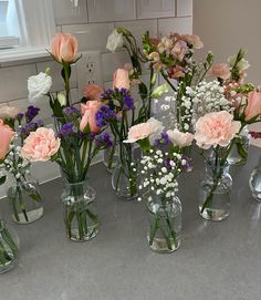 several vases filled with different types of flowers on a counter top in front of a window