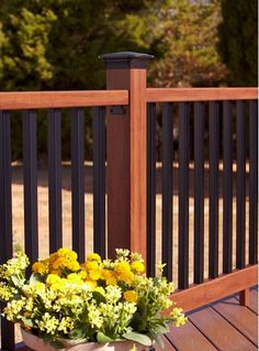 yellow flowers are in a basket on a wooden deck near a railing with black posts