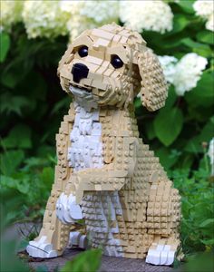 a dog made out of legos sitting on the ground in front of some flowers