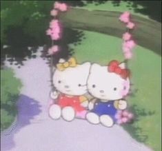 two hello kitty dolls sitting next to each other on a swing in front of flowers