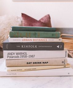 a stack of books sitting on top of a white table next to a brown pillow