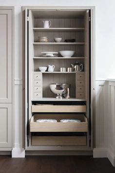 an open cabinet with dishes and cups on it's shelves in a room that has wood flooring