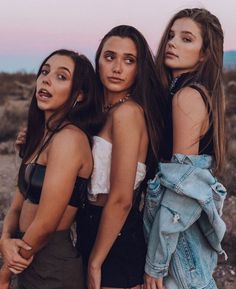 three women standing next to each other in front of a desert landscape at sunset or sunrise