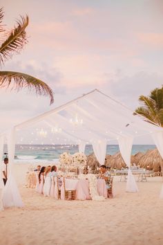 an outdoor wedding setup on the beach with white linens and draping over it