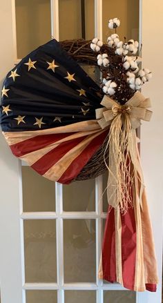 a wreath with an american flag and cotton flowers hanging on the front door to celebrate the fourth of july