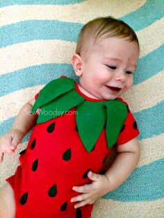 a baby laying on top of a blue and white striped rug wearing a red strawberry costume