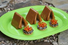 four little houses made out of chocolate on a green plate next to rocks and pebbles