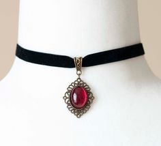 Indulge in the dark elegance of the Victorian era with this enchanting choker, crafted from luxurious black velvet ribbon and adorned with an antique bronze filigree pendant housing a blood-red glass cabochon. Perfect for enhancing your Gothic vampire aesthetic, this necklace is a timeless accessory. Key Features: Material: Black velvet ribbon and antique bronze filigree pendant with blood-red glass cabochon Choker Length: 12 inches (30.5cm), 0.4 inches (10mm) wide Pendant Size: Approximately 1 Antique Adjustable Choker As Gift, Gothic Pendant Choker As A Gift, Adjustable Gothic Necklace For Formal Occasion, Steampunk Choker Jewelry Gift, Adjustable Vampire Style Choker As Gift, Adjustable Vampire Style Choker For Gift, Vampire Style Adjustable Choker As Gift, Gothic Pendant Choker For Party, Gothic Adjustable Choker For Formal Occasions