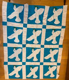 a blue and white quilt with an owl on it's back, sitting on a wooden floor