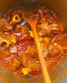 a wooden spoon in a pot filled with meat and pasta sauce on top of a table