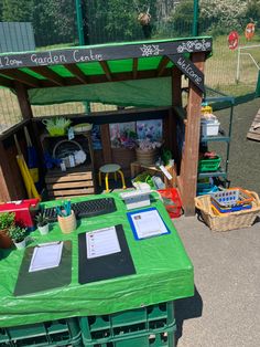 a green table topped with lots of items next to a fenced in area filled with potted plants