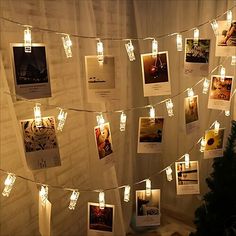 many candles are lit on the wall with pictures attached to it and strung by string lights