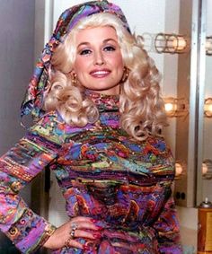 a woman with blonde hair wearing a colorful dress and posing in front of a mirror