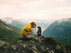 a woman kneeling down next to a dog on top of a mountain