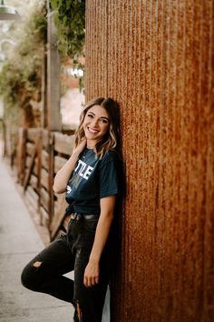 a woman leaning against the side of a wooden fence smiling and looking at the camera