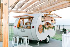 a food truck parked under a wooden structure with tables and stools on the side