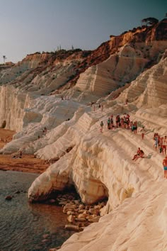 many people are standing on the edge of a cliff by the water and sand cliffs