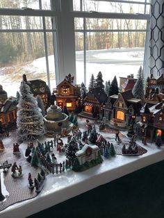 a table topped with lots of small christmas village figurines next to a window