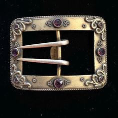 a silver belt buckle with pink stones in the center and two white pins sticking out of it