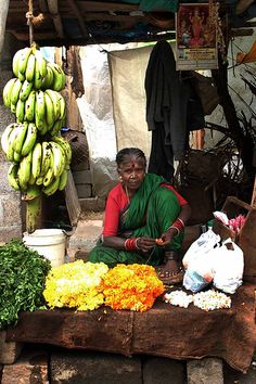 a woman sitting in front of a fruit and vegetable stand