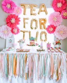 a table topped with lots of paper flowers and balloons in the shape of letters that spell out tea for two