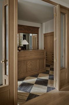 an empty room with wooden furniture and checkered flooring is seen through the open door