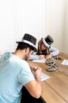 two people sitting at a table with hats on their heads and papers in front of them