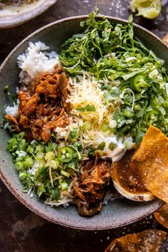 a bowl filled with meat and vegetables next to tortilla chips on a table