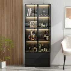 a glass door cabinet with bottles and glasses on it next to a white chair in a living room