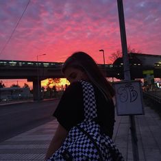 a woman carrying a checkered bag on the side of a road at sunset or dawn