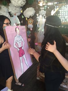 two women standing next to each other in front of a painting on a wooden floor