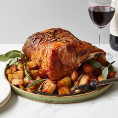 a plate with meat and potatoes on it next to a glass of wine