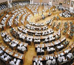 a large room filled with lots of people sitting at desks and standing in front of them