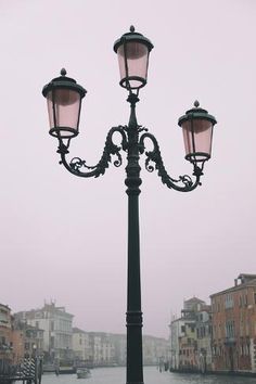 an old fashioned lamp post on the side of a river in venice, italy with buildings and boats behind it