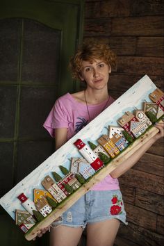 a woman holding a large wooden sign with houses painted on it