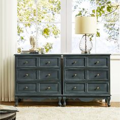 a blue dresser sitting in front of a window with a lamp on top of it