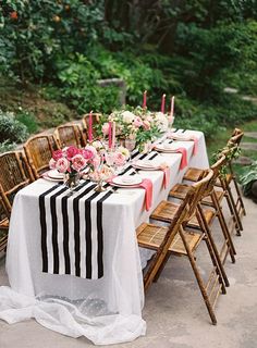 an outdoor table set up with black and white linens, pink flowers and candles