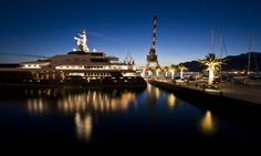 a large boat is docked in the water at night with palm trees and other boats