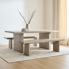 a wooden table with two benches next to it on a rug in front of a window