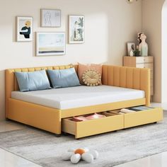 a yellow daybed with two drawers underneath it and pictures on the wall behind it