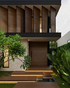 a modern house with wooden steps leading up to the front door and green plants on either side