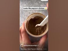 someone is holding a cup of brown stuff with a spoon in it and the text looks like popcorn chicken