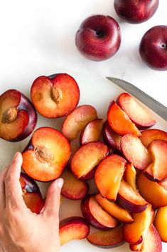 someone cutting up peaches with a knife on a cutting board next to some plums