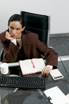 a woman sitting at a desk in front of a computer with a book and pen