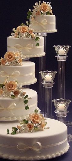 three tiered wedding cake with flowers and candles on the side, sitting next to each other